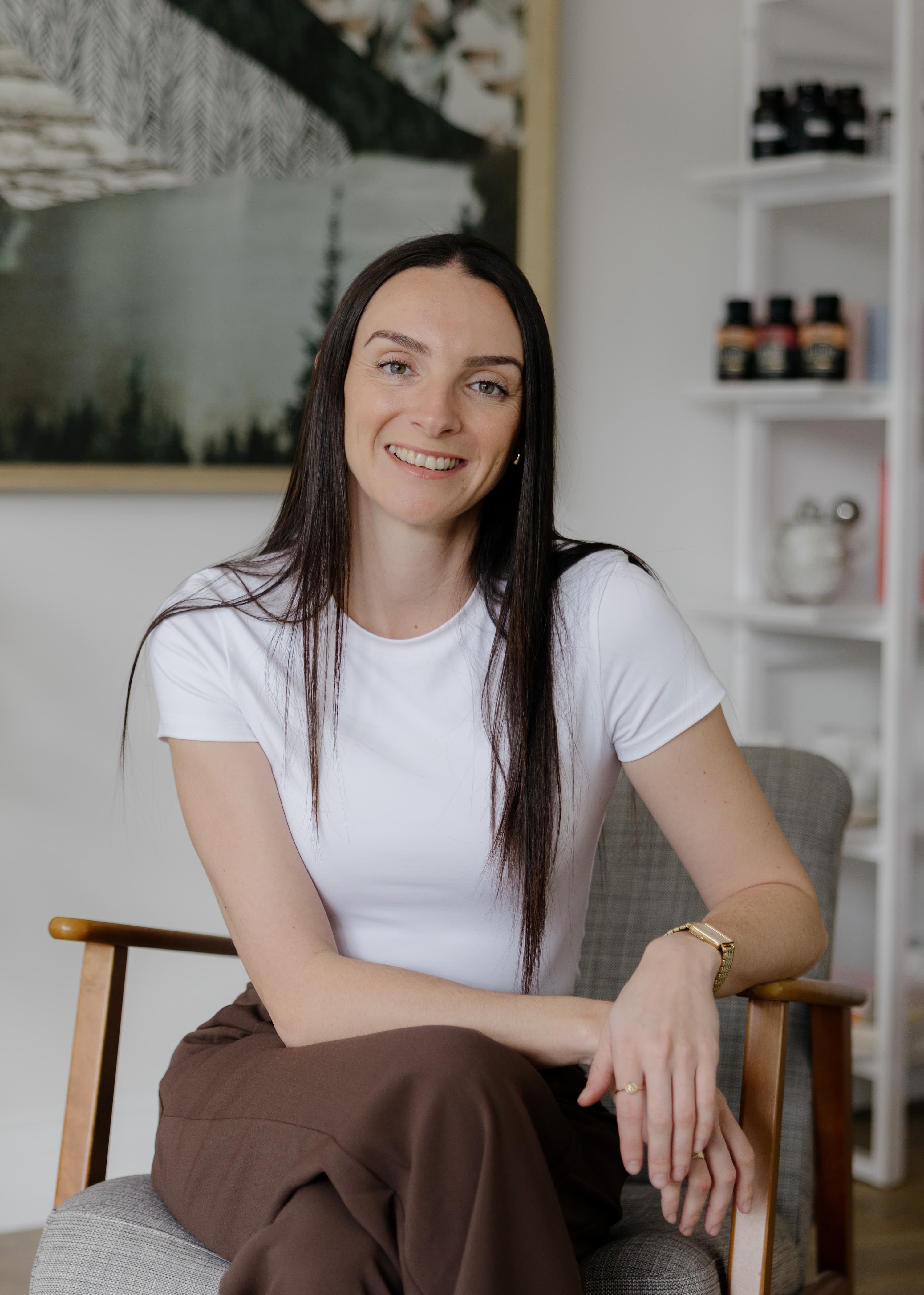 Woman sitting in a chair wearing a white shirt and brown pants in a room with decor elements at Vyne Health Acupuncture Gold Coast Clinic